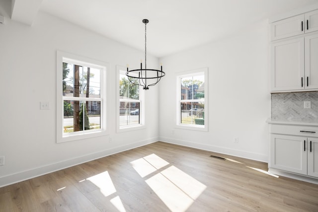 unfurnished dining area with an inviting chandelier and light hardwood / wood-style floors