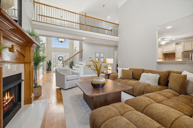 living room with a towering ceiling, a high end fireplace, and light hardwood / wood-style flooring