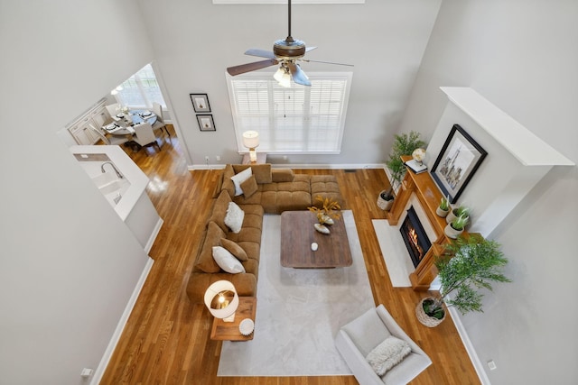 living room with ceiling fan, a towering ceiling, a wealth of natural light, and wood-type flooring