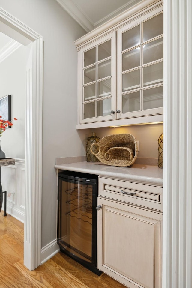 bar with beverage cooler, light wood-type flooring, and crown molding