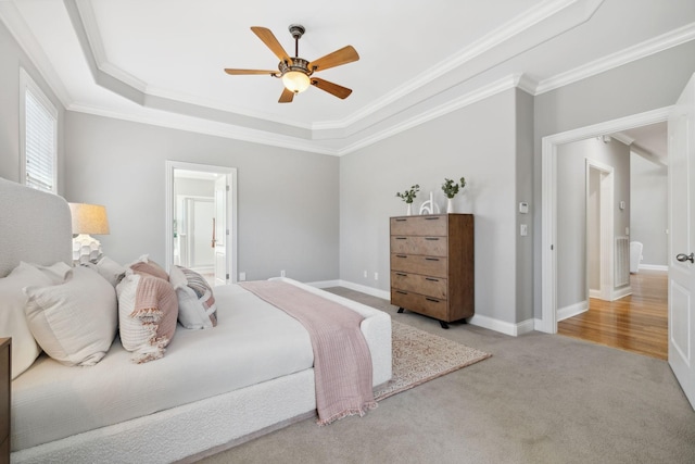 carpeted bedroom with ensuite bathroom, ceiling fan, crown molding, and a tray ceiling