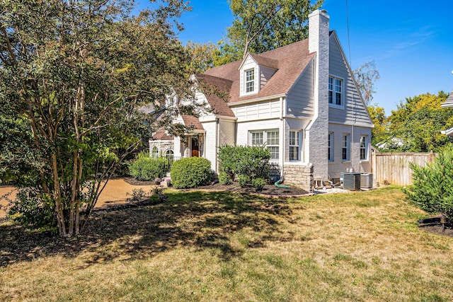 view of front of property featuring a shingled roof, a front lawn, fence, central air condition unit, and a chimney