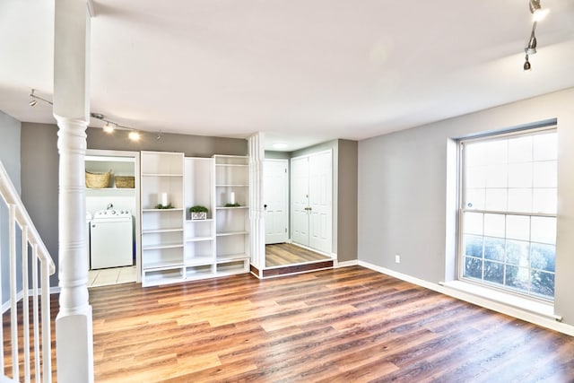 unfurnished living room with hardwood / wood-style flooring, rail lighting, and washer / dryer