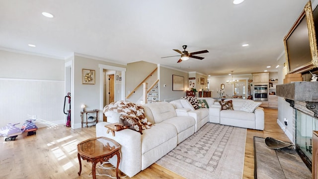 living room featuring ceiling fan with notable chandelier, light wood-type flooring, and crown molding