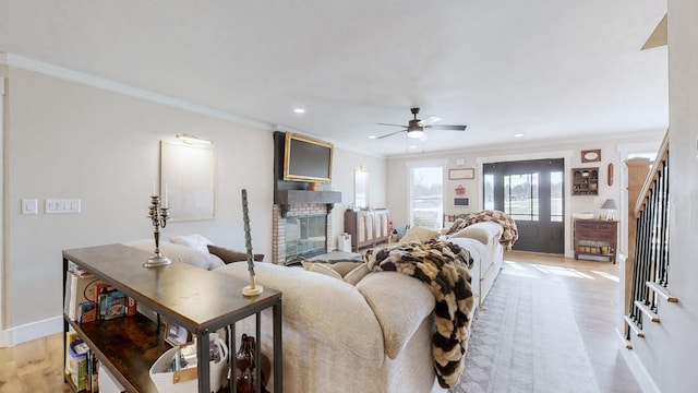 living room with a fireplace, light wood-type flooring, ceiling fan, and crown molding