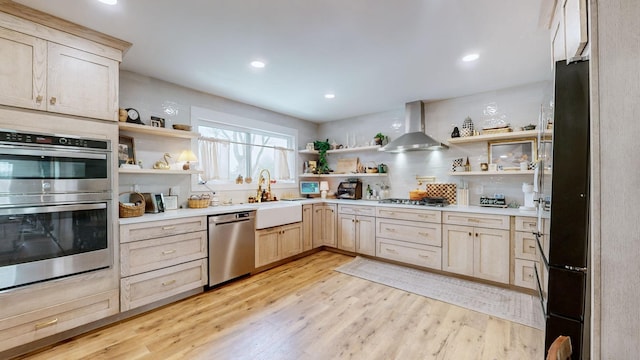 kitchen with stainless steel appliances, light hardwood / wood-style flooring, wall chimney range hood, and light brown cabinetry