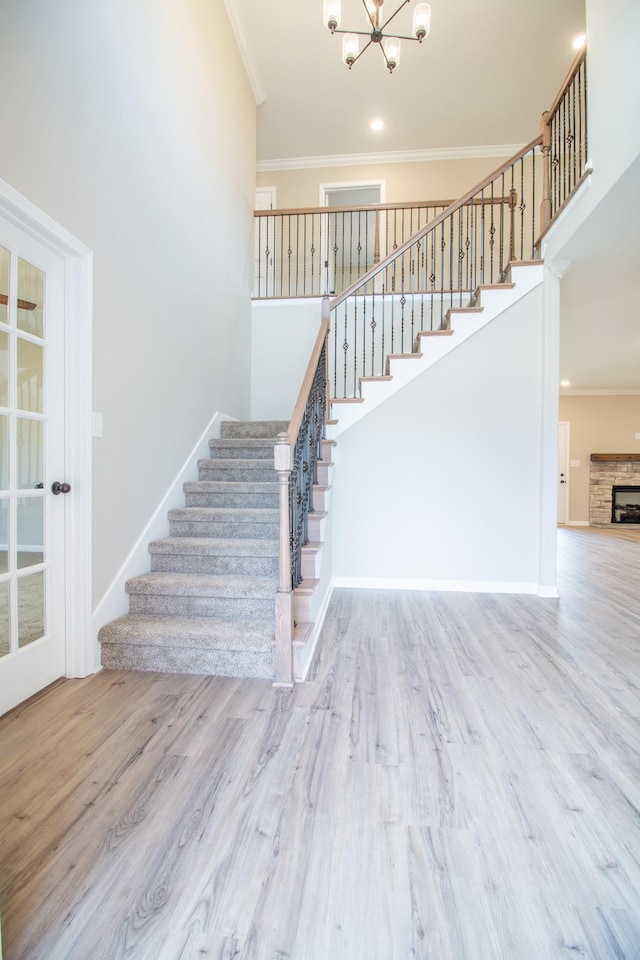 stairs with a notable chandelier, crown molding, a fireplace, and wood-type flooring