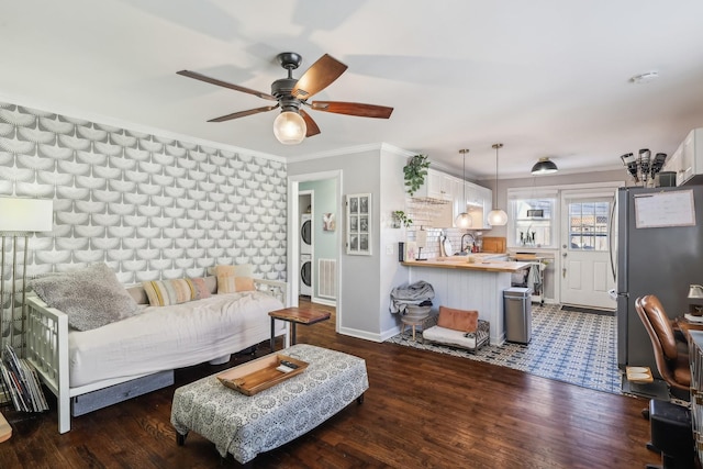 living room featuring stacked washer and dryer, sink, crown molding, and dark wood-type flooring