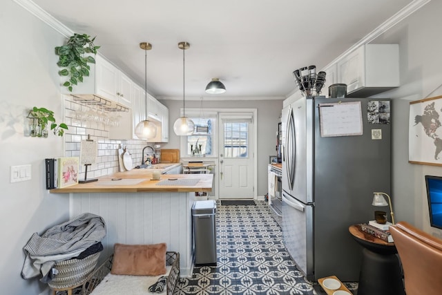 kitchen featuring stainless steel refrigerator, kitchen peninsula, pendant lighting, butcher block countertops, and white cabinetry