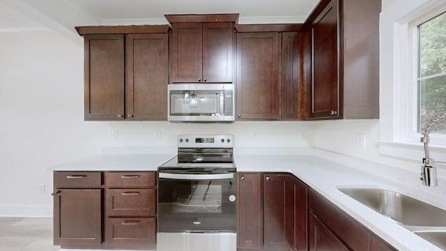 kitchen featuring stainless steel appliances, sink, dark brown cabinets, and light stone counters