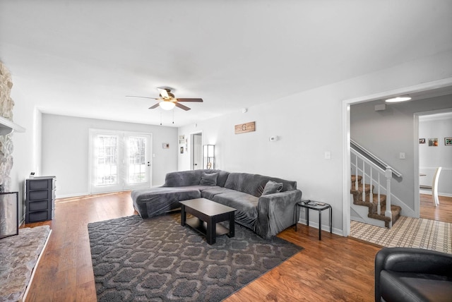 living room with ceiling fan, dark wood-type flooring, and a stone fireplace