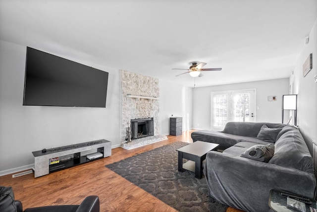 living room featuring ceiling fan, hardwood / wood-style flooring, and a stone fireplace