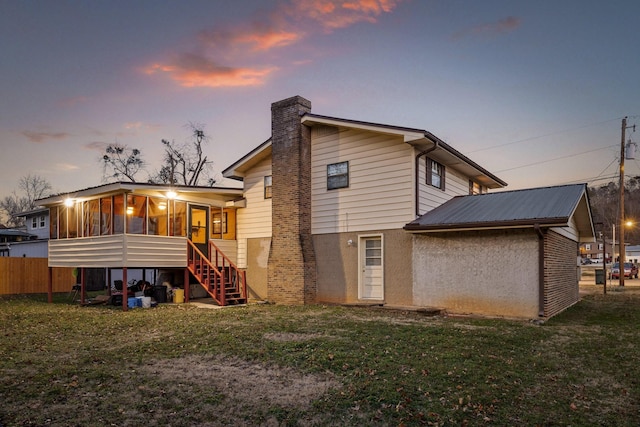 back house at dusk with a lawn and a sunroom