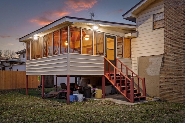 back house at dusk featuring a sunroom and a lawn