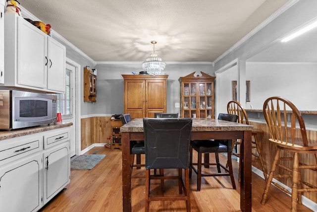 dining space with crown molding, light hardwood / wood-style flooring, wood walls, and a notable chandelier