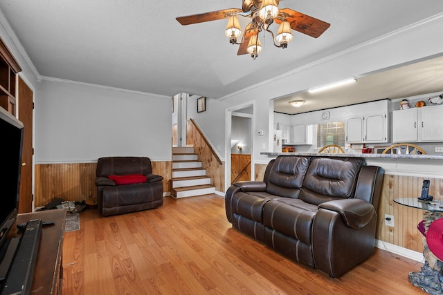 living room with a textured ceiling, light hardwood / wood-style flooring, ornamental molding, and wooden walls