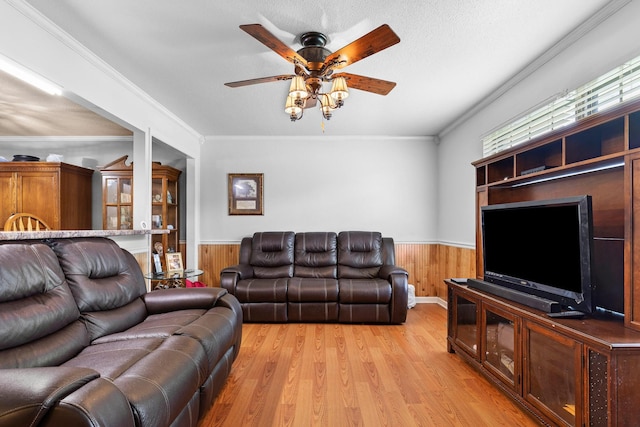 living room featuring light wood-type flooring, ceiling fan, ornamental molding, and a textured ceiling