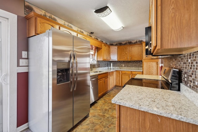 kitchen with stainless steel appliances, sink, a textured ceiling, light stone counters, and tasteful backsplash