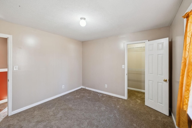 unfurnished bedroom with a walk in closet, a textured ceiling, a closet, and carpet flooring