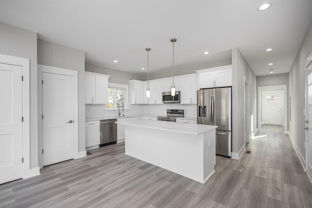 kitchen featuring hanging light fixtures, a kitchen island, white cabinets, appliances with stainless steel finishes, and sink