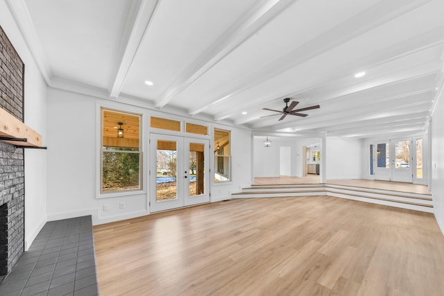 unfurnished living room featuring a brick fireplace, ceiling fan, light wood-type flooring, french doors, and beam ceiling