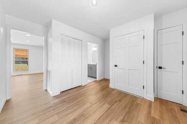 unfurnished bedroom with multiple closets, connected bathroom, and light hardwood / wood-style flooring