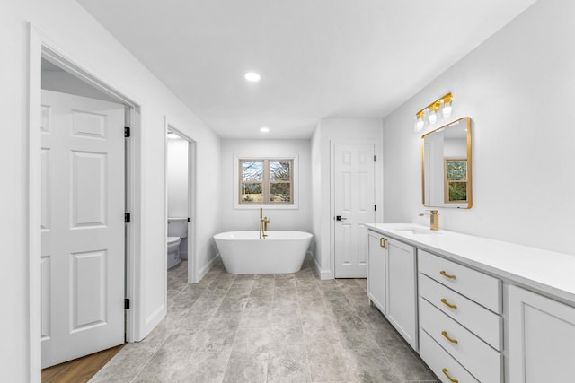 bathroom with a tub to relax in, vanity, and toilet