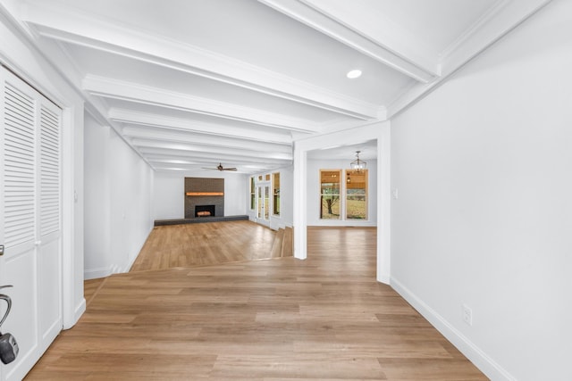 unfurnished living room with ceiling fan, a large fireplace, beamed ceiling, and light hardwood / wood-style floors