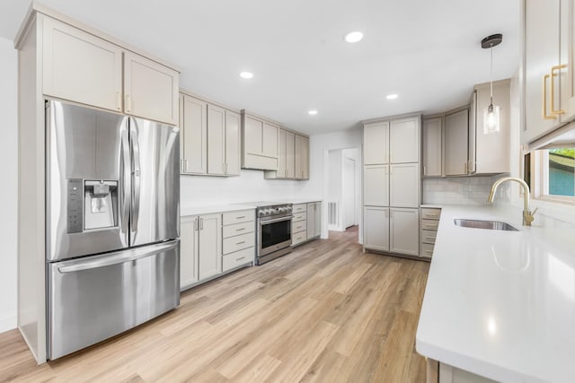 kitchen featuring appliances with stainless steel finishes, gray cabinetry, light wood-type flooring, hanging light fixtures, and sink