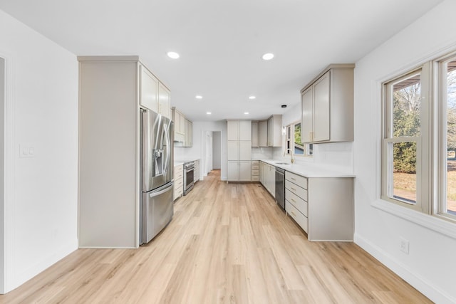 kitchen with backsplash, gray cabinets, sink, light wood-type flooring, and appliances with stainless steel finishes