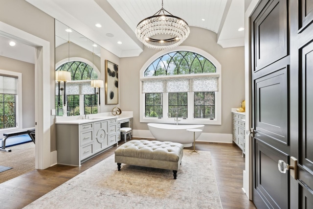 bathroom with an inviting chandelier, a tub, vanity, and wood-type flooring