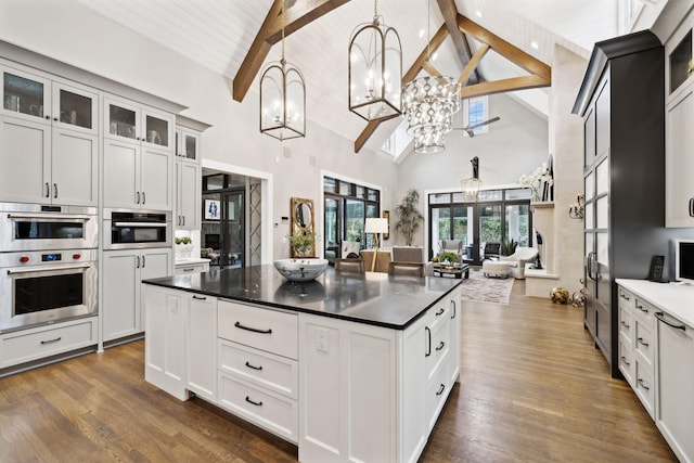 kitchen with decorative light fixtures, dark hardwood / wood-style floors, high vaulted ceiling, double oven, and beam ceiling