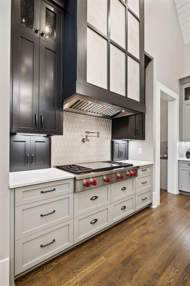 kitchen featuring dark wood-type flooring, wall chimney exhaust hood, tasteful backsplash, stainless steel gas cooktop, and white cabinets