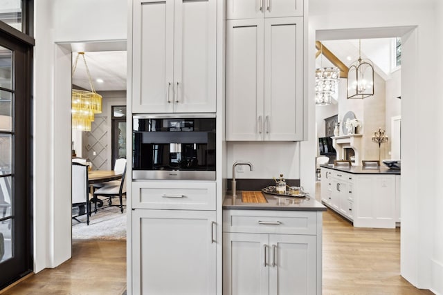 kitchen with decorative light fixtures, stainless steel oven, white cabinets, and light hardwood / wood-style flooring