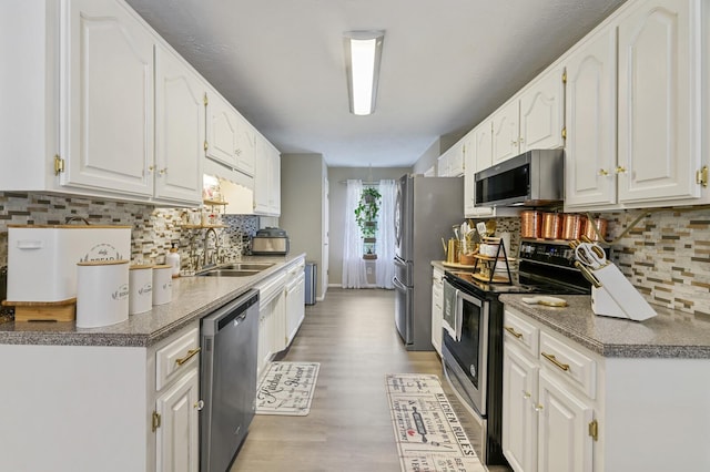 kitchen featuring decorative backsplash, light wood-type flooring, white cabinetry, appliances with stainless steel finishes, and sink