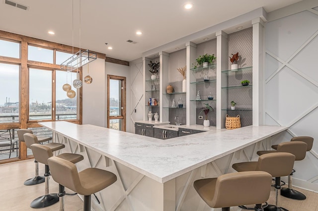 kitchen featuring light hardwood / wood-style floors, built in features, kitchen peninsula, a breakfast bar area, and hanging light fixtures