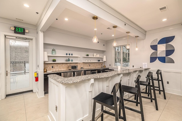 kitchen featuring a breakfast bar area, kitchen peninsula, light stone counters, decorative light fixtures, and tasteful backsplash