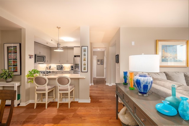 kitchen with light hardwood / wood-style flooring, pendant lighting, stainless steel appliances, a breakfast bar area, and sink