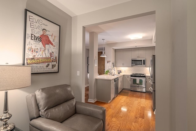 kitchen featuring stainless steel appliances, decorative light fixtures, light wood-type flooring, decorative backsplash, and gray cabinetry