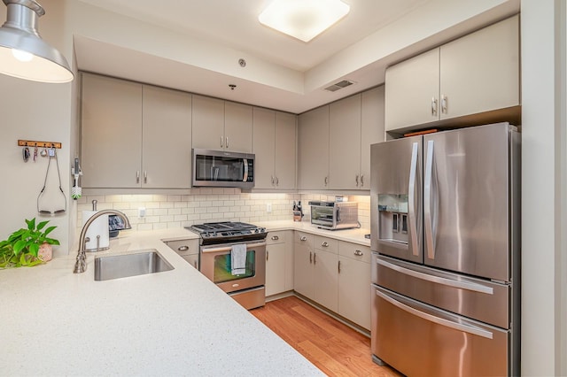 kitchen featuring gray cabinets, light hardwood / wood-style floors, stainless steel appliances, sink, and tasteful backsplash