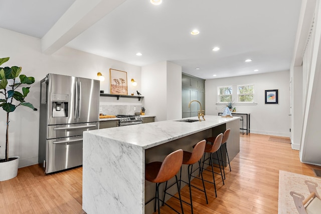 kitchen featuring light stone counters, an island with sink, light wood-type flooring, appliances with stainless steel finishes, and sink