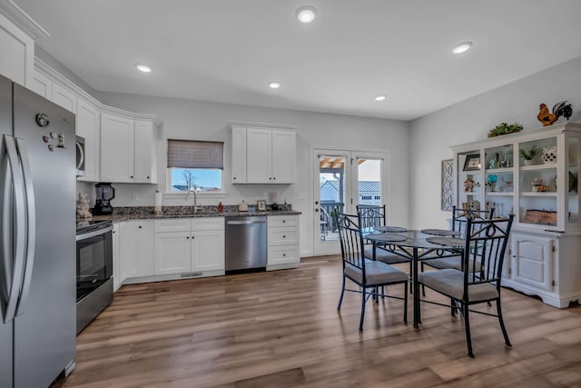 kitchen with wood-type flooring, appliances with stainless steel finishes, dark stone counters, sink, and white cabinetry