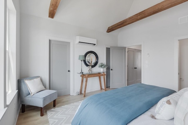 bedroom with light wood-type flooring, beam ceiling, and a wall mounted air conditioner