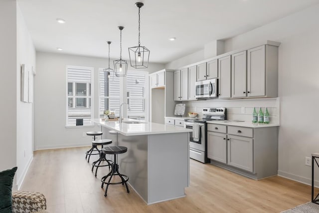 kitchen featuring stainless steel appliances, sink, an island with sink, hanging light fixtures, and gray cabinets