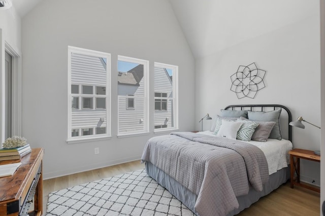 bedroom with light wood-type flooring and high vaulted ceiling