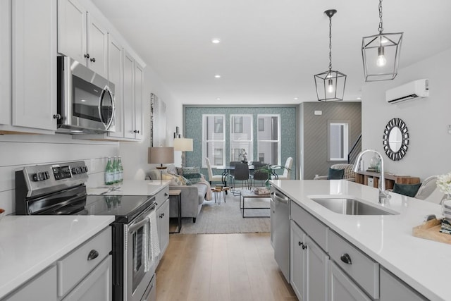 kitchen with sink, decorative light fixtures, white cabinetry, an AC wall unit, and appliances with stainless steel finishes