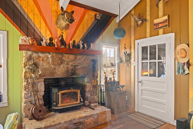 living room featuring hardwood / wood-style flooring, wooden walls, lofted ceiling with beams, and a wood stove