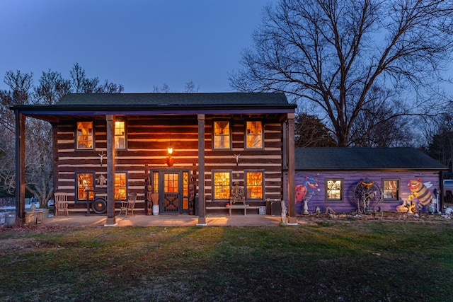 back house at dusk with a patio and a lawn