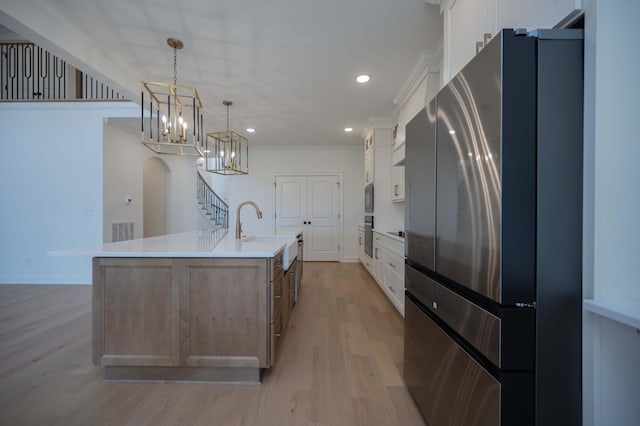 kitchen with decorative light fixtures, a large island, white cabinets, ornamental molding, and stainless steel refrigerator