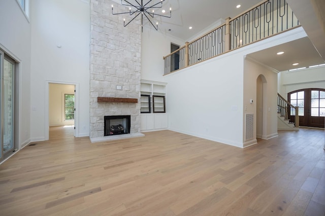 unfurnished living room featuring a towering ceiling, ornamental molding, french doors, a fireplace, and light hardwood / wood-style flooring